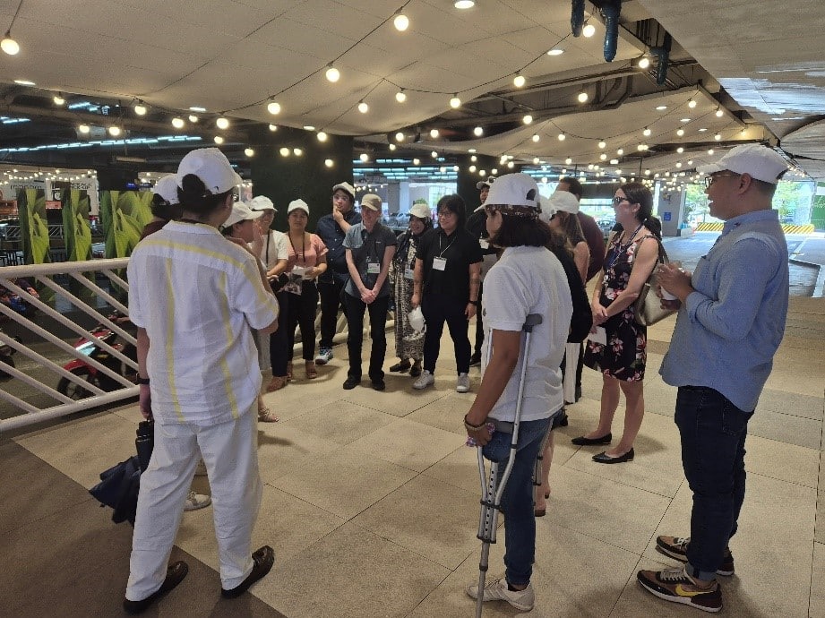 The image shows participants of the Jane's Walk standing together, all wearing white caps with the Women on the Move logo.